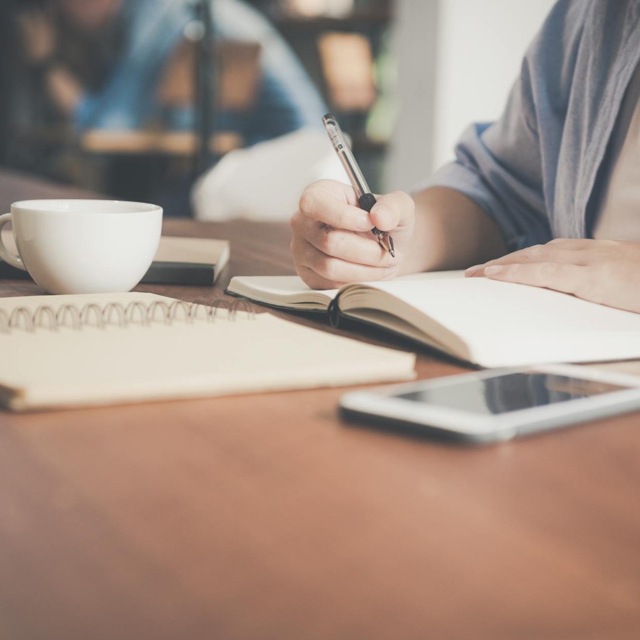 woman writing on a notebook beside teacup and tablet computer